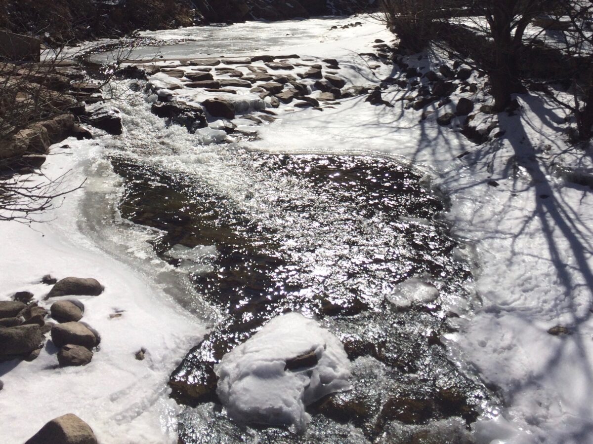 Ice-rimmed creek side with waterfalls flowing down over rocks in Boulder Creek. 