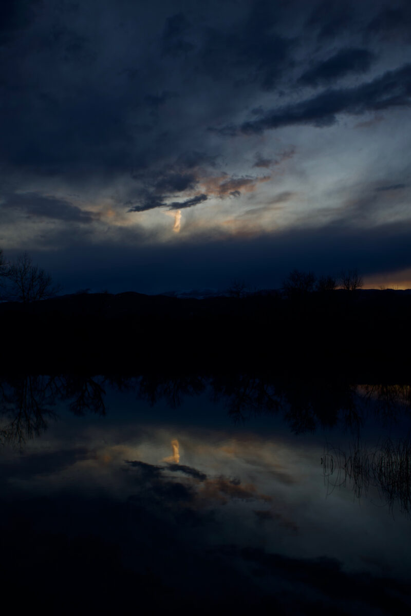 an image of ethereal light, an angel in darkening clouds with a reflection of the light shape in water below