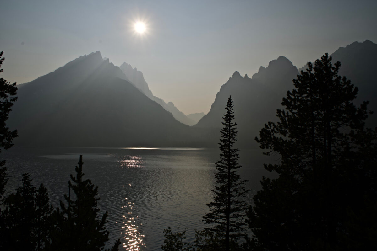 Title: Grief and Hope. An image of Jenny Lake in the Grand Tetons, where smoke and haze obscure the sun and cloud the mountains in the evening sunset. 